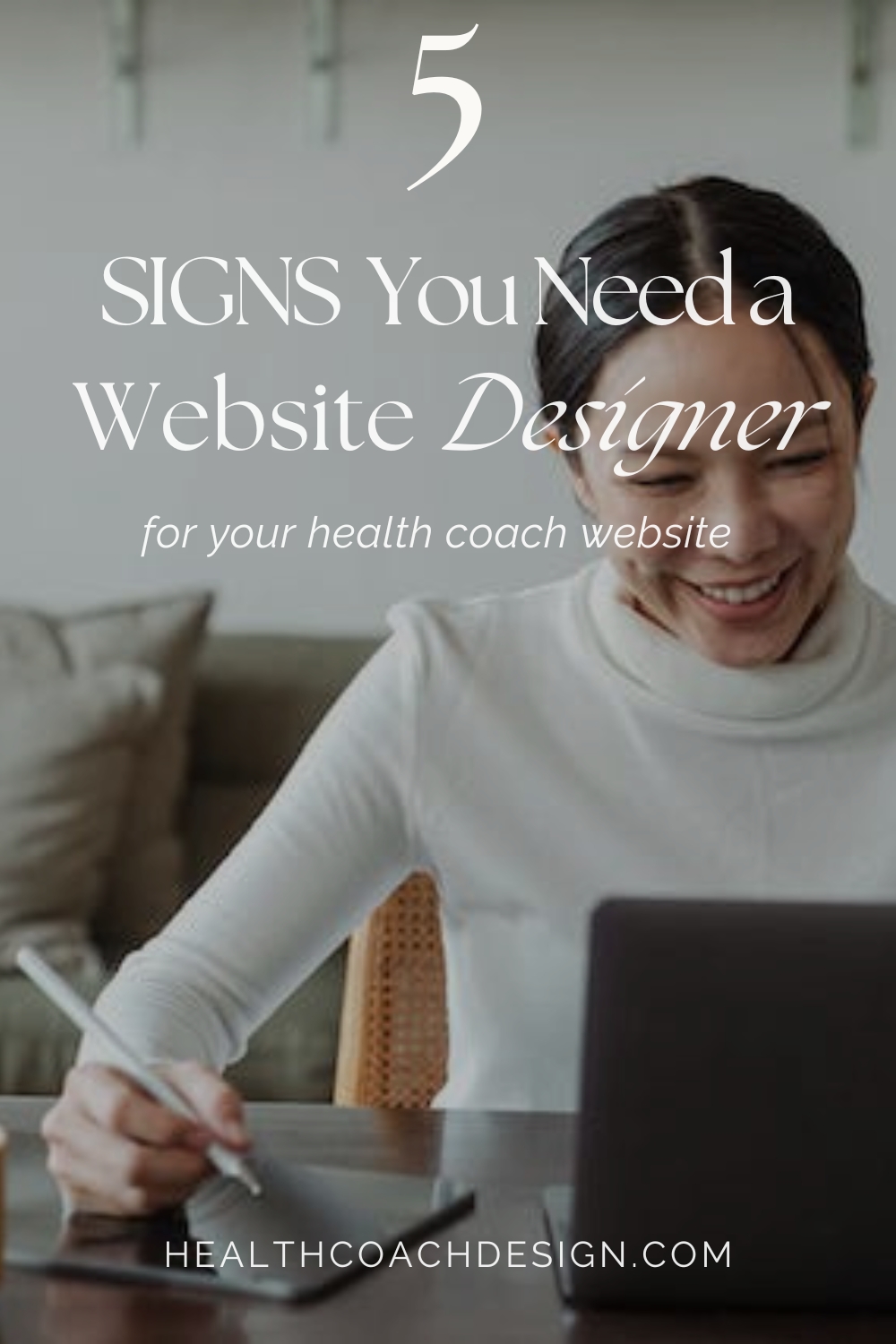 Pinterest pin for blog post titled "5 Signs You Need a Website Designer for Your Health Coach Website." Woman in photo is sitting looking at a laptop screen on a desk and writing with a digital pen on a tablet that's laying flat on a desk.