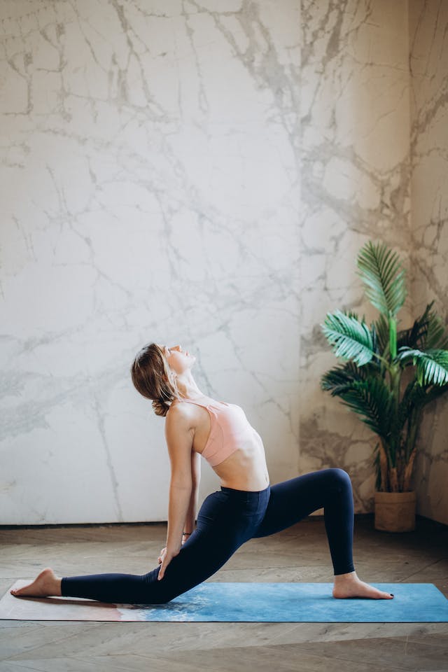 Woman on mat stretching with plant behind her.